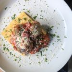 white plate with polenta and meatballs with sauce