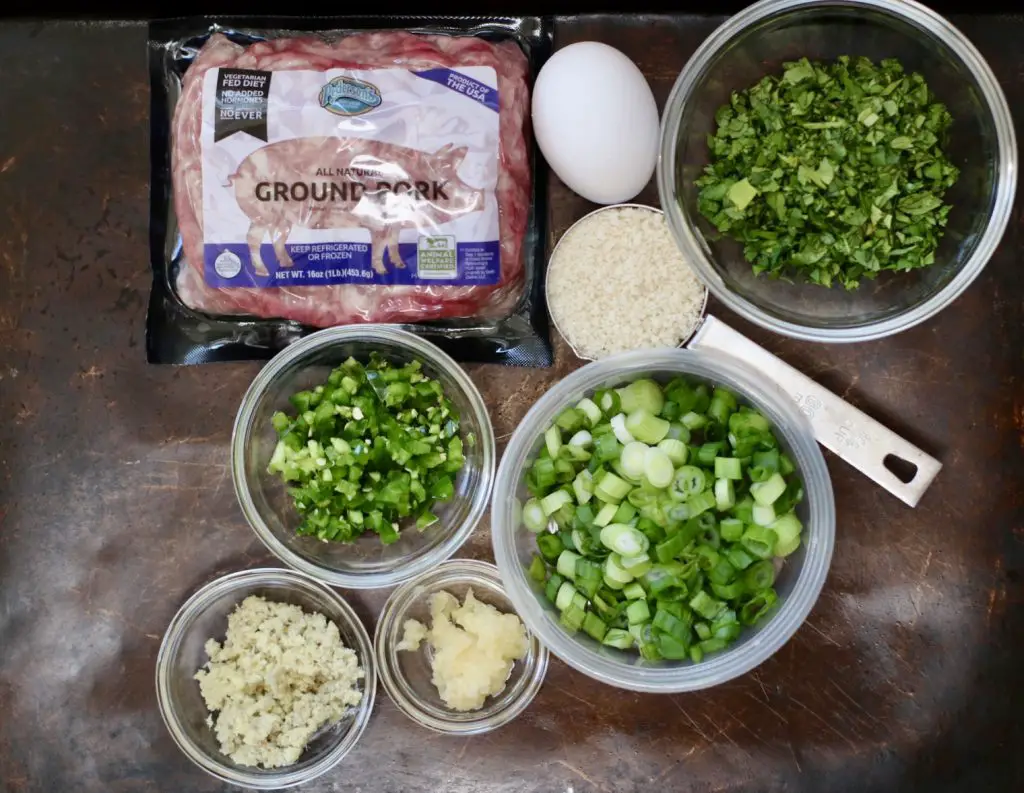 A flat lay of fresh ingredients for coconut curry meatballs, including ground pork, fresh herbs, green onions, jalapeño, garlic, and ginger.